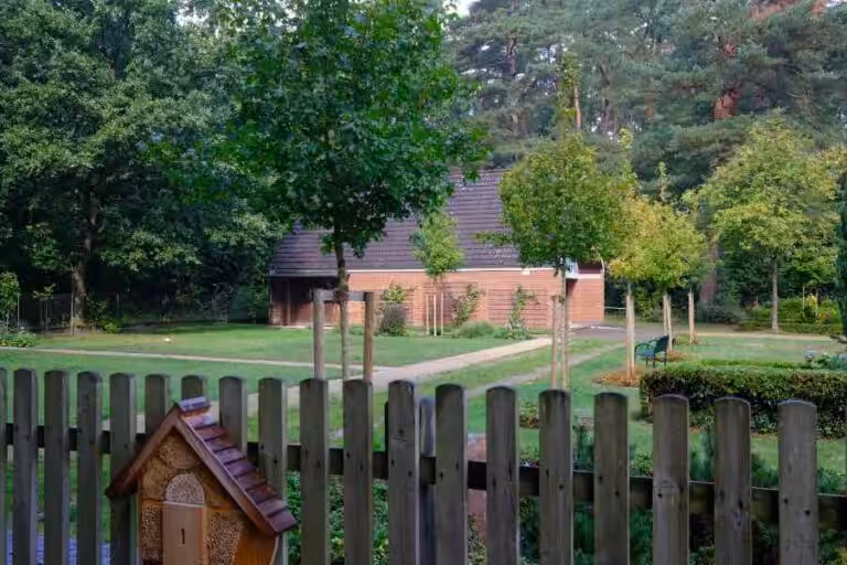 Garten mit Holzzaun und Bäumen, Gebäude im Hintergrund.