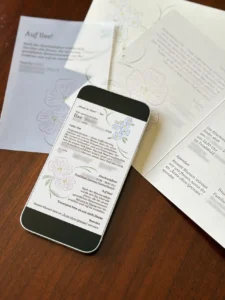 Smartphone mit Traueranzeige neben gedruckten Trauerkarten